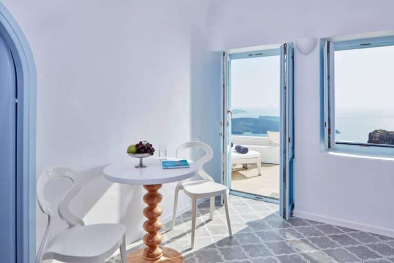 Sitting area with a round table and doors open to the terrace at Astra Suites, Imerovigli, Santorini