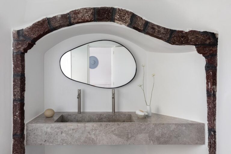 Stone-arched bathroom with a carved basin and oval mirror at Canaves Oia Suites, Oia, Santorini