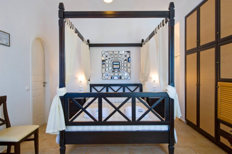 Bedroom with a dark wood four-poster bed at Chora Resort Hotel & Spa, Folegandros