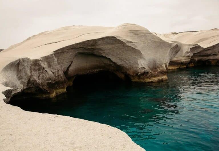 White volcanic rock arch above clear water on the Milos coast at Domes White Coast, Mytakas, Milos