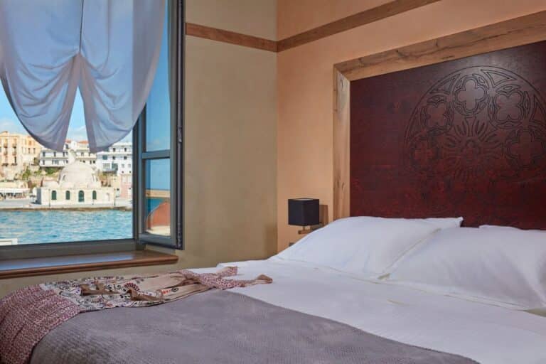 Bedroom with a carved headboard and a window onto the harbour at Domus Renier, Chania, Crete